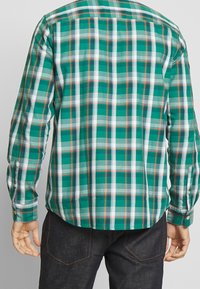 Grønternet skjorte med knapper, hvide og orange accenter, lange ærmer, buet kant og knaplukning ved ærmerne. Fremstillet af letvægtsstof.