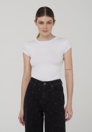 Body corto bianco a maniche corte realizzato in tessuto elastico, design aderente. Indossato con pantaloni in denim neri a vita alta con dettagli in perle.