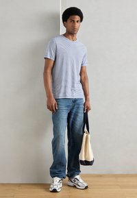 Tricou cu mânecă scurtă și dungi, de culoare albastru deschis, asortat cu blugi albaștri. Modelul ține o geantă de pânză crem cu bleumarin. Adidașii au accente gri și negre.
