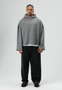 Grijze oversized hoodie met een brede hals en verlaagde schoudernaden, gecombineerd met losse zwarte jeans en stevige zwarte sneakers.