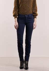 Granatowe skinny jeans o gładkiej fakturze, z detalami w postaci paneli na kolanach i dopasowanym kroju. Połączone z teksturowanymi czarnymi botkami na wysokim obcasie.