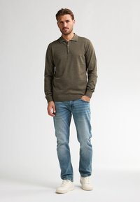Polo shirt verde oliva a maniche lunghe con colletto, dotato di tre bottoni. Abbinato a jeans azzurri e sneakers bianche.
