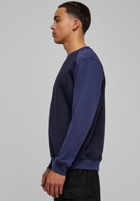 Tumesinise värvusega pusa, mis on valmistatud pehmest kangast, millel on ümara kaelusega kaelus, pikad varrukad, soonikkoes mansetid ja lõdvalt istuv lõige.