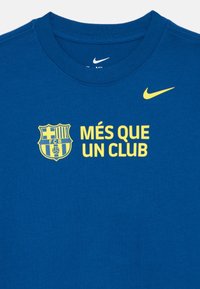 Μπλε βαμβακερό T-shirt με στρογγυλή λαιμόκοψη. Διαθέτει κίτρινο κείμενο "MÉS QUE UN CLUB" και το έμβλημα της FC Barcelona στο μπροστινό μέρος. Λογότυπο Nike σε κίτρινο χρώμα.