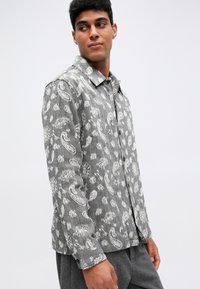 Hallus hallilt särgil, millel on valged paisleimustrid, nööbid ees, krae ja pikkade varrukatega, mis on nööpidega kinnitatud. Sile kangastekstuur.