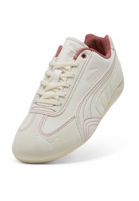 Zapatillas de ante crema con acentos en rosa, que cuentan con un diseño de cordones, suela moldeada y un logotipo de Puma elevado en el lateral para un detalle adicional.