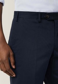 Pantaloni blu navy con una texture liscia, dotati di un'unica chiusura a bottone e tasche laterali. Il tessuto presenta un design classico e una vestibilità sartoriale.