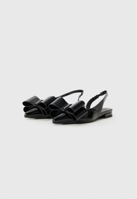 Čierne lakované slingback topánky s špicatými prstami a výraznými nadrozmernými mašľami vpredu. Nízky plochý opätok, hladká textúra.