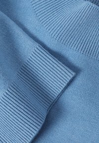 Pull tricoté bleu clair à texture lisse, avec des accents côtelés aux poignets et à l'encolure, présentant un design en couches.