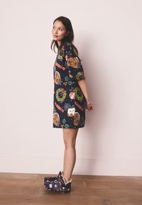 Tengerészkék ruha, színes ünnepi motívumokkal, puha, mintás papuccsal, szőrmével díszítve. Lapos talpú cipő és sima textúra.