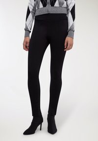 Leggings nere in materiale elastico, con una vita alta e un design elegante, abbinati a stivaletti neri con punta.