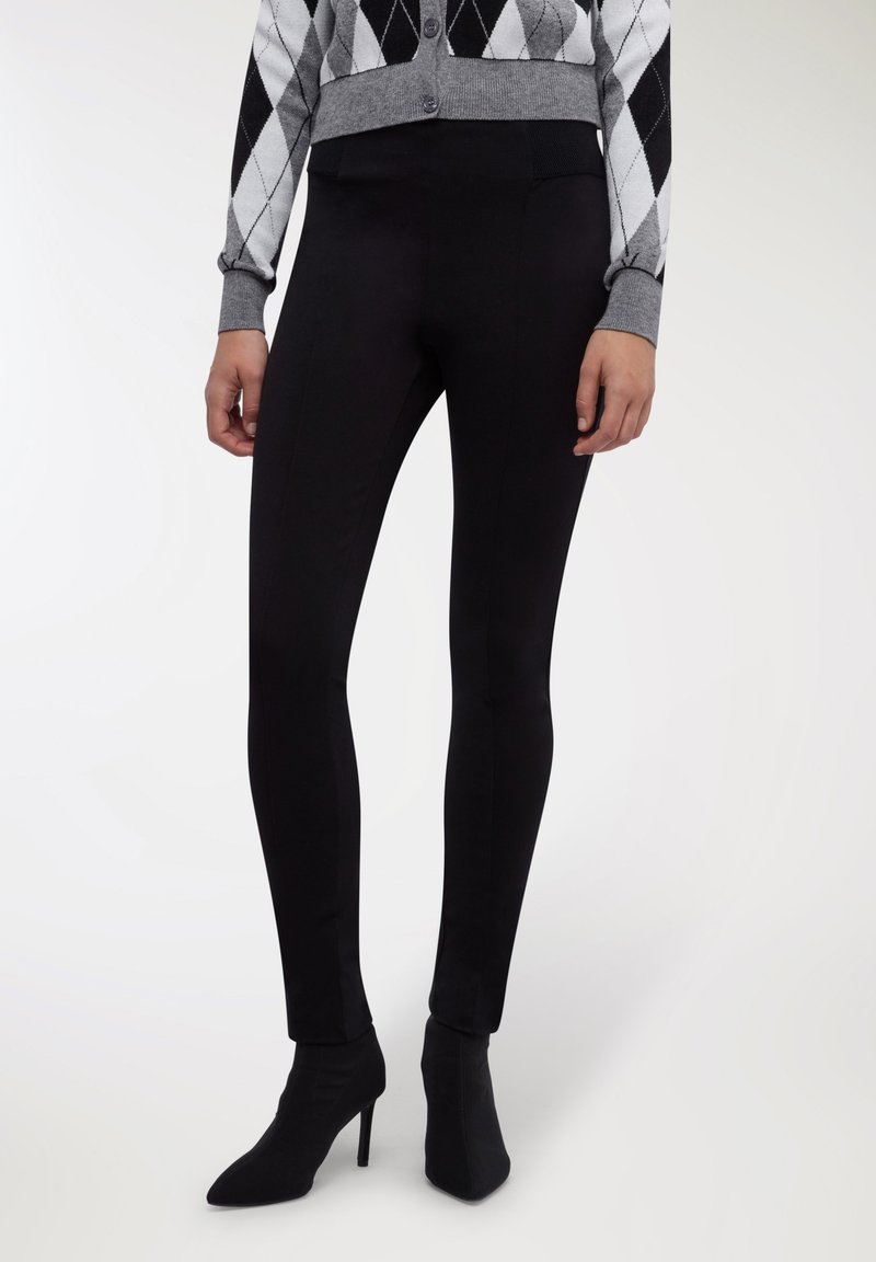 Leggings nere in materiale elastico, con una vita alta e un design elegante, abbinati a stivaletti neri con punta.