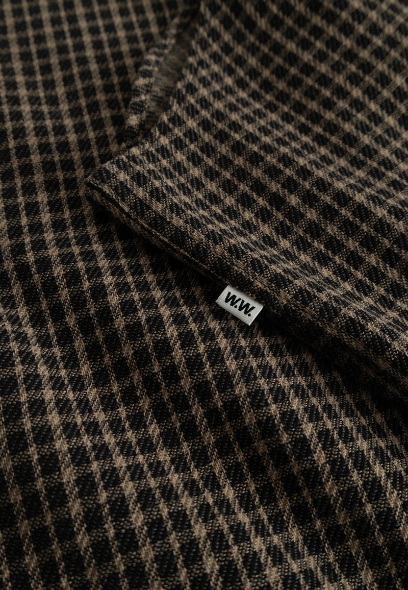 Tessuto misto lana con un motivo a scacchi in nero e marrone. Presenta un bordo ripiegato e un piccolo etichetta tessuta con "W.W." nell'angolo in basso.