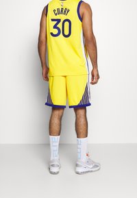 Maillot de basketball jaune avec des accents bleus, numéro 30 dans le dos, associé à un short jaune assorti et des chaussettes blanches avec un texte bleu.
