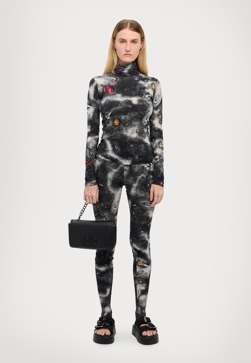 Bodysuit de estampado de galaxia en negro y gris con mangas largas y cuello alto; combinado con un bolso minimalista negro y sandalias gruesas.