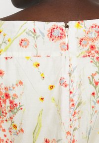 Blommig klänning i lättviktigt tyg med vit bakgrund, prydd med färgglada blommönster i röd, gul och grön. Detalj med dragkedja bak.