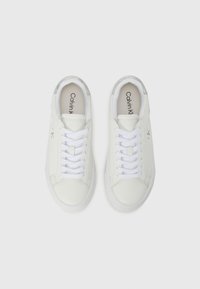 Sneaker bianche in pelle con finitura liscia, dotate di lacci bianchi, suole in gomma e un leggero accento metallico sul tallone. Marchio Calvin Klein all'interno.