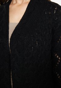 Cardigan nero lavorato a maglia con frontale aperto, motivo testurizzato e vestibilità ampia con design a treccia.