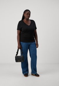 Camiseta negra de cuello en V combinada con jeans de pierna ancha azules, sosteniendo un bolso negro con un logo dorado, con una textura suave y un ajuste entallado.