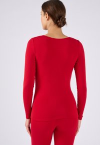 Maglia rossa a maniche lunghe con scollatura rotonda, forma aderente e tessuto liscio. Il design presenta spalle senza cuciture e una finitura morbida.