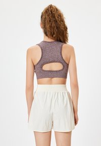 Mauve urheiluliivi, jossa on urheilupaita-malli ja leikattu yksityiskohta. Yhdistetty kevyisiin, teksturoituihin, kermaisiin shortseihin, joissa on elastinen vyötärö.