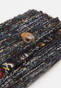 Černá a vícebarevná kabelka z tvídu s výrazným zlatým zapínáním zdobeným drahokamy, které má tvar oka. Texturovaný, obdélníkový tvar.