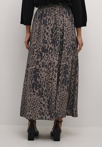 Maxi sukňa v béžovej farbe s čiernym leopardím vzorom. Elastický pás, splývavy strih a textúrovaná tkanina. Viditeľné čierne členkové topánky.