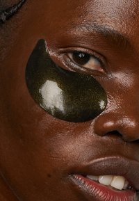 Grüne Gel-Augenmasken auf der Haut, gebogene Form, glatte Textur, reflektierendes Licht. Natürlicher Hautton mit leichtem Glanz, der die Platzierung des Produkts hervorhebt.