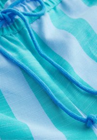 Gros plan sur un tissu rayé bleu et turquoise avec un cordon bleu noué à la taille élastique.