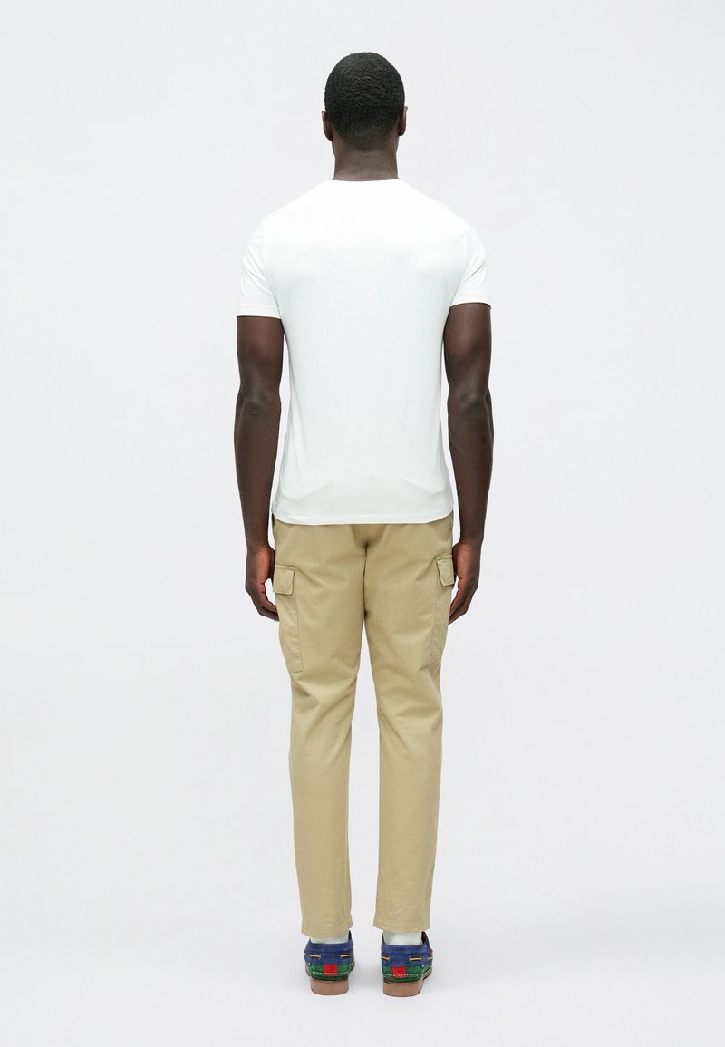 T-shirt bianca a maniche corte, pantaloni cargo beige con tasche laterali e sandali multicolore. Design semplice, vestibilità comoda e palette di colori neutri.