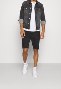 Černá džínová bunda s ohrnutými rukávy, bílý tričko, černé roztrhané šortky a bílé tenisky. Jednoduchý, ale moderní volnočasový outfit.