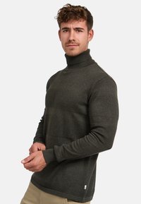 Mørkegrønn strikket høyhalset genser med strukturerte horisontale striper og ribbestrikkede mansjetter. Mykt stoff med en tettsittende silhuett.