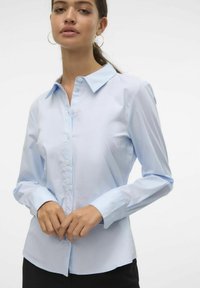 Camisa de manga larga azul claro con cierre de botones, cuello puntiagudo y diseño ajustado. Tejido suave y forma entallada, con puños de botón.