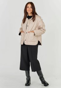 Bež jackhall, millel on suured nööbid ja küljetaskud, koos mustade laia säärega pükste ja mustade põlvikuni saapadega; sile tekstuur.