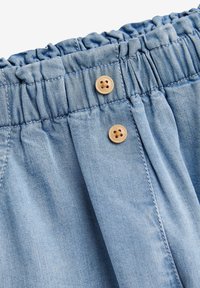 Indumento in denim blu chiaro con vita elastica bordata di volant e due bottoni in legno sul davanti.
