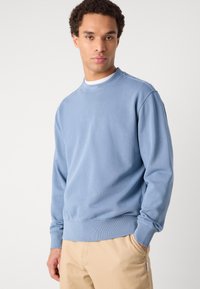 Ανοιχτό μπλε φούτερ με στρογγυλή λαιμόκοψη και ραφές στους καρπούς και στο τελείωμα. Διαθέτει διακριτική επωνυμία στον λαιμό. Φτιαγμένο από μαλακό ύφασμα.