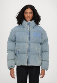 Gaišzils džinsu pūkainā jakas ar augstu apkakli, priekšu ar rāvējslēdzēju un divām sānu kabatām; rotā neliels "Moschino Jeans" logo zilā krāsā.