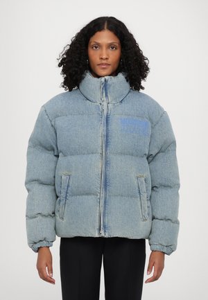 Denim puffer jakna u svijetloplavoj boji s visokim ovratnikom, prednjim zatvaračem i dva bočna džepa; sadrži diskretan "Moschino Jeans" logo u plavoj boji.