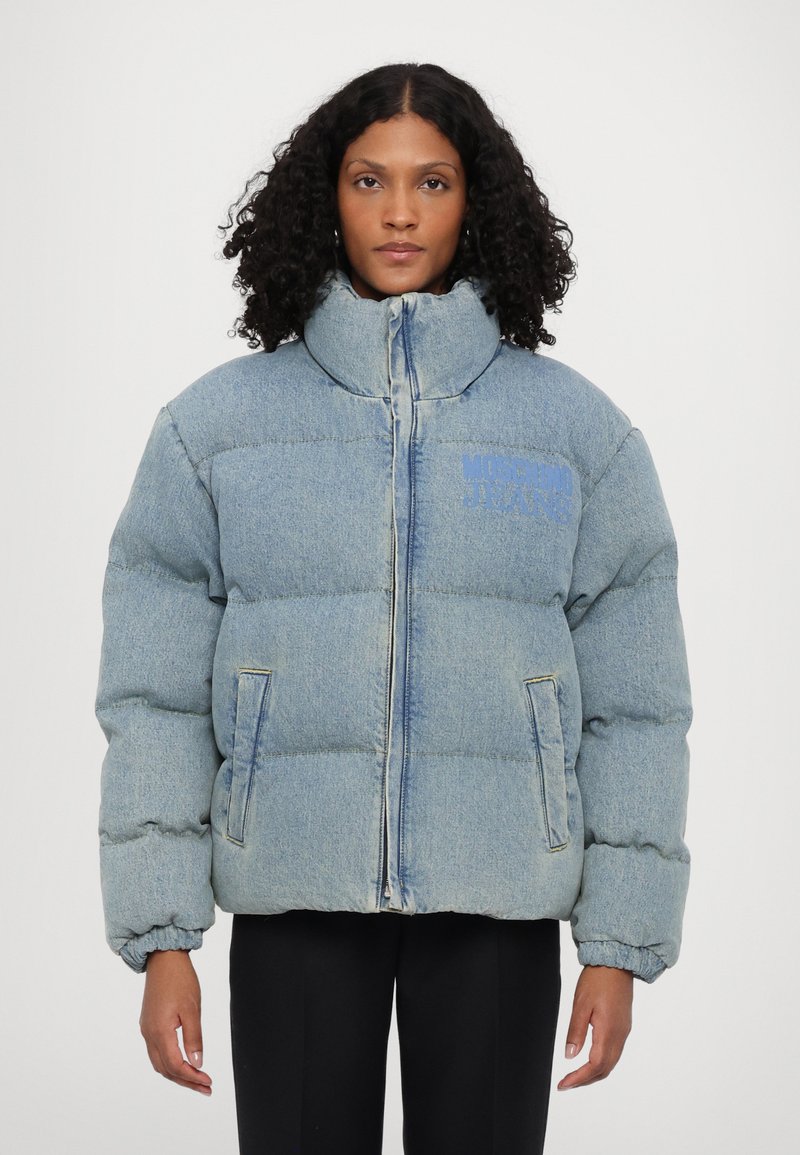 Gaišzils džinsu pūkainā jakas ar augstu apkakli, priekšu ar rāvējslēdzēju un divām sānu kabatām; rotā neliels "Moschino Jeans" logo zilā krāsā.