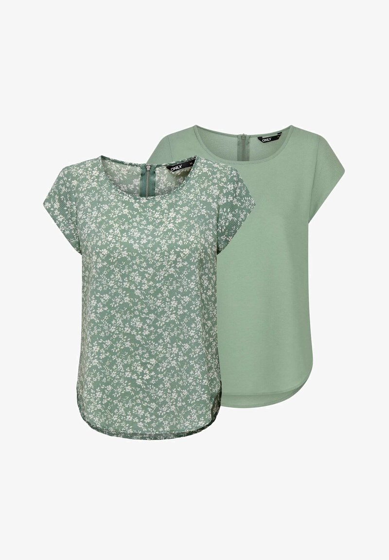 Zwei grüne Oberteile sind ausgestellt, eines mit einem kleinen Blumenmuster und kurzen Ärmeln, das andere einfarbig grün mit einem runden Halsausschnitt und einem Reißverschluss auf dem Rücken.