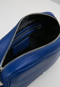 Borsa in pelle blu con esterno texture, chiusura con zip e fodera nera. All'interno presenta una piccola tasca con zip e un'etichetta del marchio.