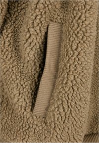 Bruine fleecejas met een textuur, voorzien van een geribbelde tan manchetten en een zijvak voor functionaliteit.