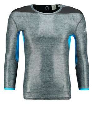 Męski model idący, ubrany w dopasowany szaro-czarny sportowy top z niebieskimi akcentami, czarne szorty z niebieskim obszyciem i szare buty do biegania.