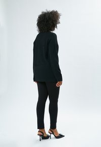 Maglione nero oversize con maniche lunghe, taglio dritto, tessuto morbido. Abbinato a leggings neri aderenti e décolleté nere con tacco e decorazioni.