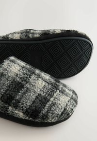 Gray and white plaid fuzzy slippers with textured upper, black rubber sole featuring geometric tread pattern, and soft plush material.