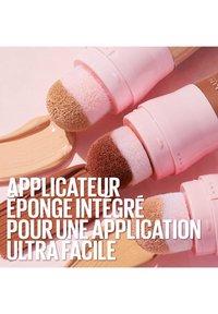 Applicateur double face avec embouts en éponge intégrés. Poignée rose clair, embouts texturés doux en rose et marron, et un échantillon de produit cosmétique lisse.