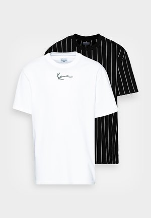 Dos camisetas: una blanca con un logo negro de firma y otra negra con rayas blancas verticales. Ambas están hechas de una tela suave y tienen mangas cortas.