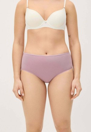 Mujer con sujetador blanco y ropa interior de talle alto color lavanda, de pie con los brazos relajados contra un fondo liso y claro.