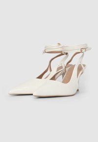 Scarpe slingback bianche con punta a punta realizzate in pelle testurizzata, con cinturino sottile alla caviglia con fibbia e tacco basso.