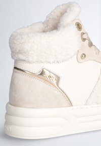 Sneaker alto crema e beige con colletto in ecopelliccia, pannelli in suede e pelle, dettagli metallici e logo sulla parte laterale.